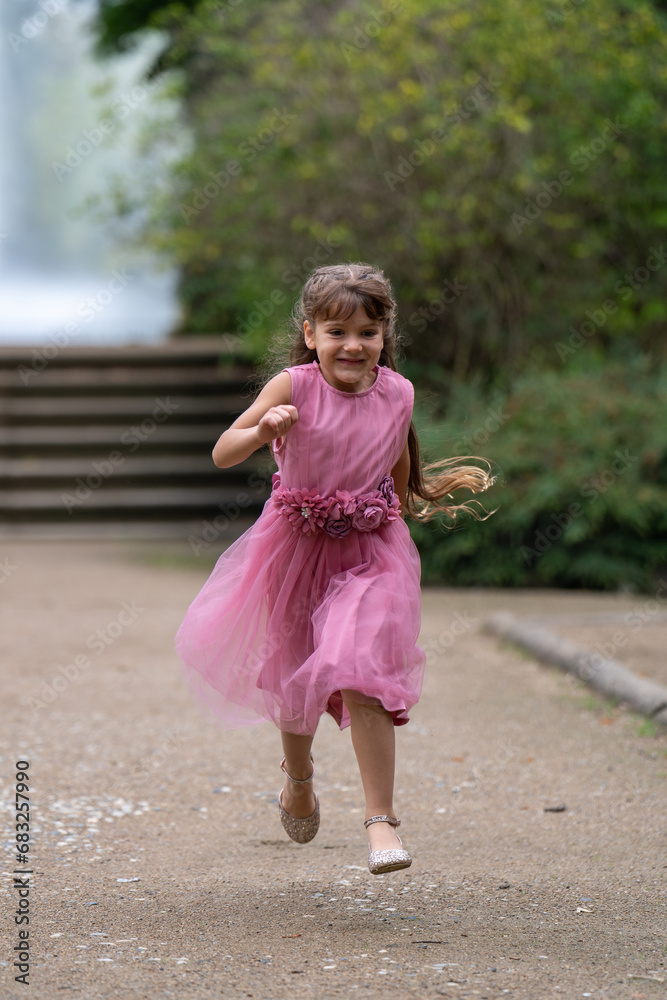 A little cute girl in a beautiful pink dress with long hair runs quickly. Outdoor games. Blurred background.