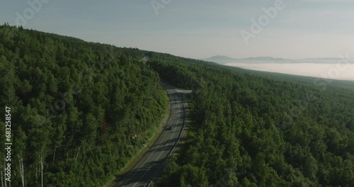 One black car driving alone road trip, travel on freeway through dense colorful forest mountains corridor at summer sunny sunset - Aerial drone wide view