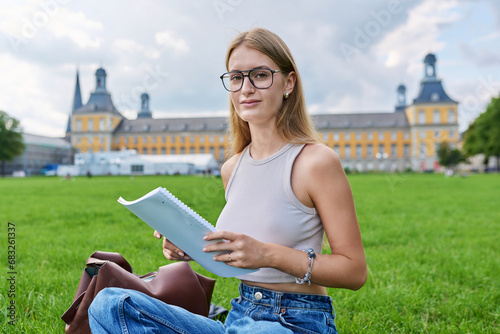 Young student girl sitting on grass, educational building background photo