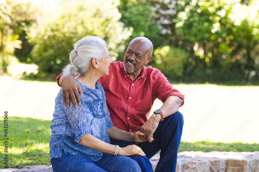 Happy diverse senior couple embracing and sitting on stairs in sunny garden Happy diverse senior couple embracing and sitting on stairs in sunny garden