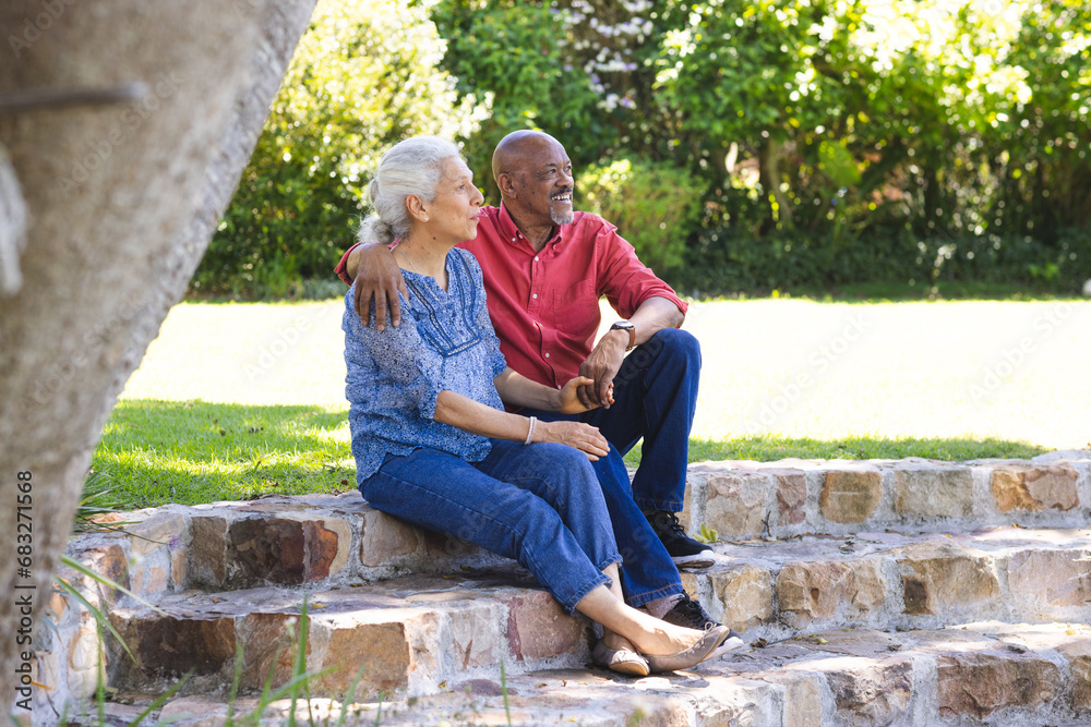 Happy diverse senior couple embracing and sitting on stairs in sunny garden Happy diverse senior couple embracing and sitting on stairs in sunny garden