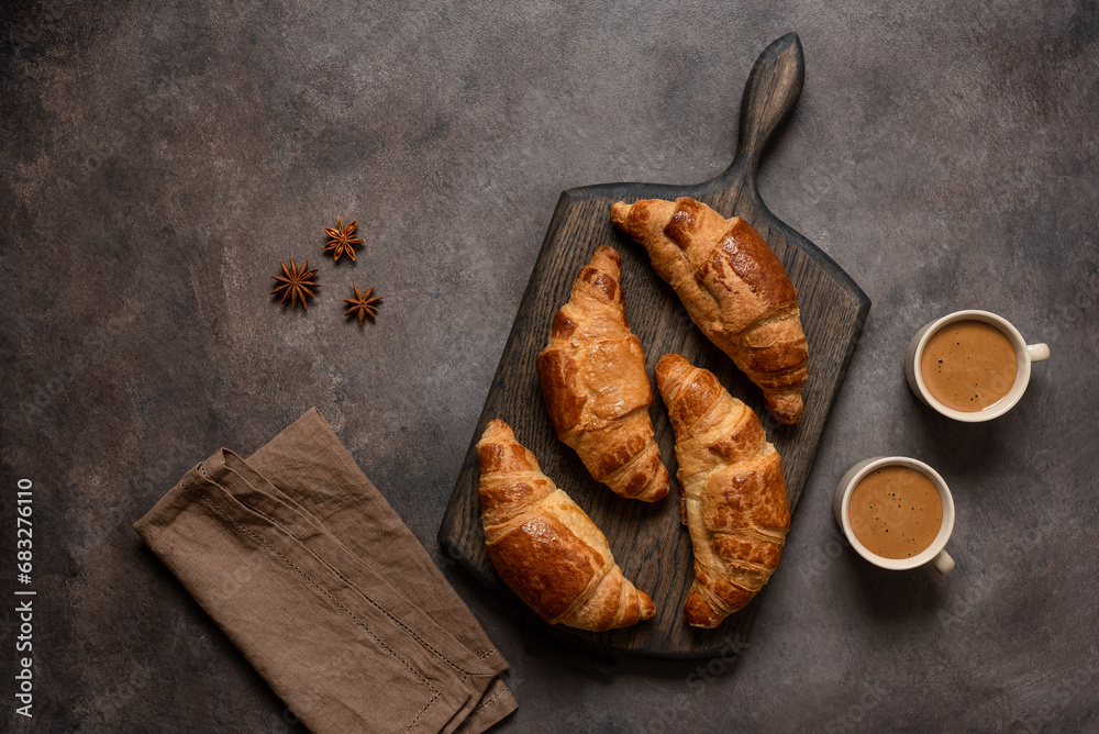 Fresh croissants and cups of coffee on a dark rustic background. Top view, flat lay. Delicious fresh breakfast.