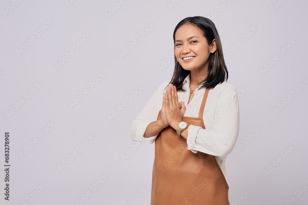Young Asian woman barista employee in brown apron working in coffee shop, holding hands together, greeting clients with smiling friendly isolated on white background. Small business startup concept Young Asian woman barista employee in brown apron working in coffee shop, holding hands together, greeting clients with smiling friendly isolated on white background. Small business startup concept