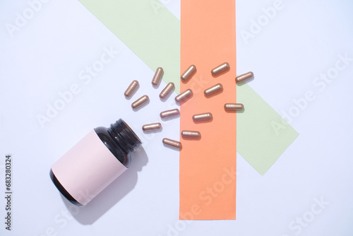 View from above of the hard capsules are poured from an unbranded pill bottle on a pastel background. Medical theme with minimalist background. Space for ads.