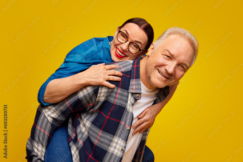 Obraz premium Smiling, beautiful happy senior woman, couple, man and woman in casual clothes posing against yellow studio background. Concept of marriage, relationship, Valentine's Day, love, emotions, fashion