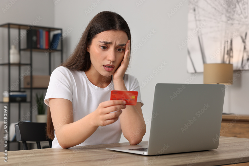 Stressed woman with credit card and laptop at table indoors. Be careful - fraud Stressed woman with credit card and laptop at table indoors. Be careful - fraud