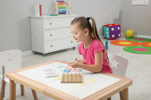 Motor skills development. Girl playing with geoboard and rubber bands at white table in kindergarten photo