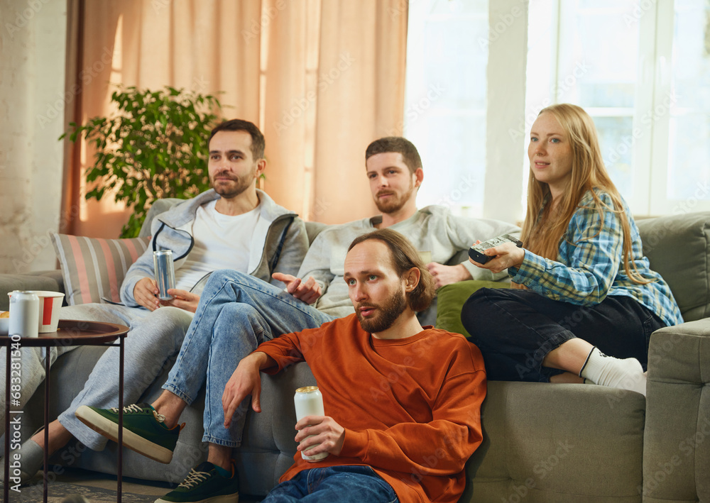Obraz premium Group portrait of guys and girl, friends and lovely couple sitting in living room and choosing genre of movie to watch.
