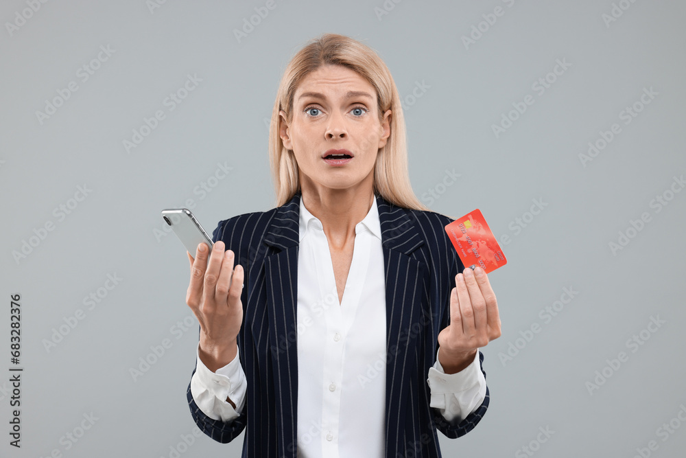 Stressed woman with credit card and smartphone on grey background. Be careful - fraud Stressed woman with credit card and smartphone on grey background. Be careful - fraud