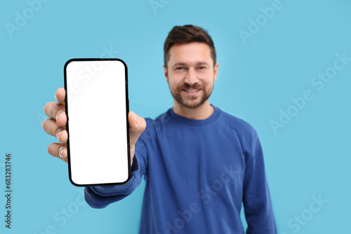 Handsome man showing smartphone in hand on light blue background, selective focus. Mockup for design