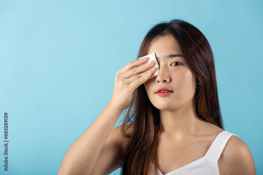 Facial Beauty Treatment Hygiene skin. Asian beautiful young woman removing cosmetic make up using pad cotton face cleaner disc, studio shot isolated on blue background, Happy female cleaning eyes Facial Beauty Treatment Hygiene skin. Asian beautiful young woman removing cosmetic make up using pad cotton face cleaner disc, studio shot isolated on blue background, Happy female cleaning eyes