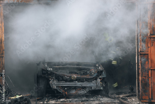 Firefighters extinguish a burning car in a garage. Burnt car. Rescuers. Strong smoke. Emergency. Insurance case.