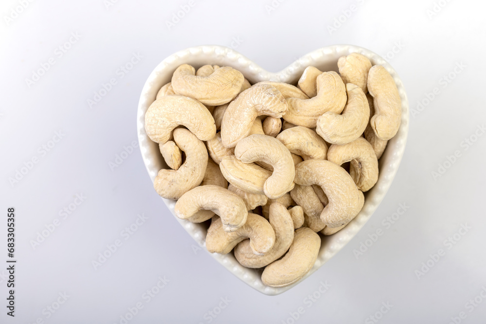 Fototapeta premium A top view of whole cashew nuts arranged beautifully in a heart-shaped bowl against a clean white background
