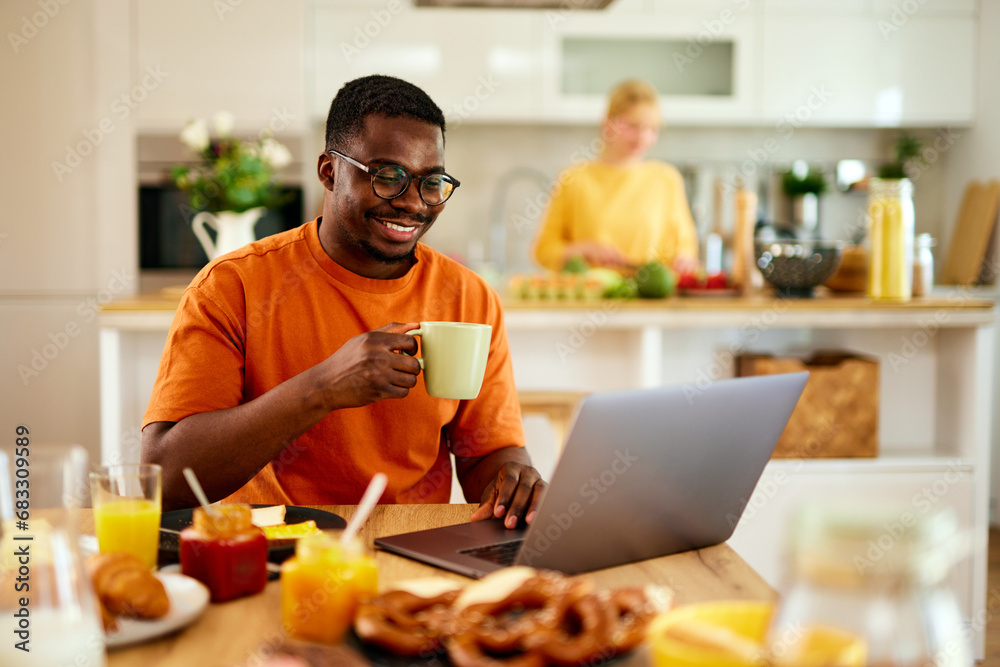 African American man using laptop while enjoying breakfast at home African American man using laptop while enjoying breakfast at home