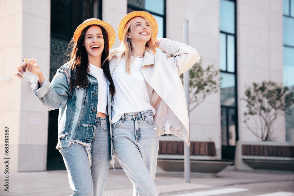 Two young beautiful smiling hipster female in trendy summer clothes. Carefree women posing in the street. Positive models having fun outdoors at sunny day. Cheerful and happy. In hat Two young beautiful smiling hipster female in trendy summer clothes. Carefree women posing in the street. Positive models having fun outdoors at sunny day. Cheerful and happy. In hat
