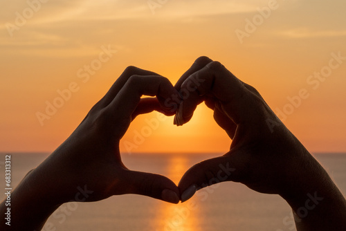 Hands heart sea sanset. The image features a beautiful sunset with two people holding their hands up in the air  forming a heart shape.