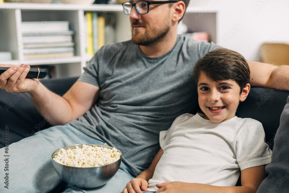 Joyful caucasian boy is watching television with his father.