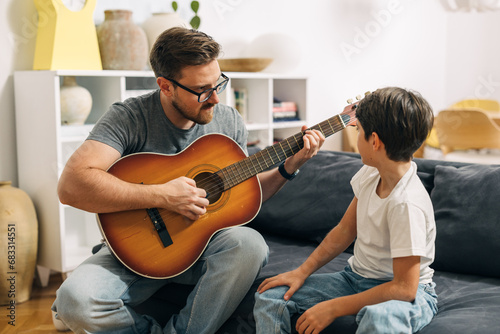 Young Caucasian boy is learning to play a guitar from his father. photo