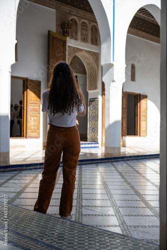 Obraz na płótnie (Selective focus) Stunning view of a tourist taking a photo at the Bahia Palace during a sunny day. The Bahia Palace in Marrakech is an impressive example of Moroccan architecture and design. w salonie
