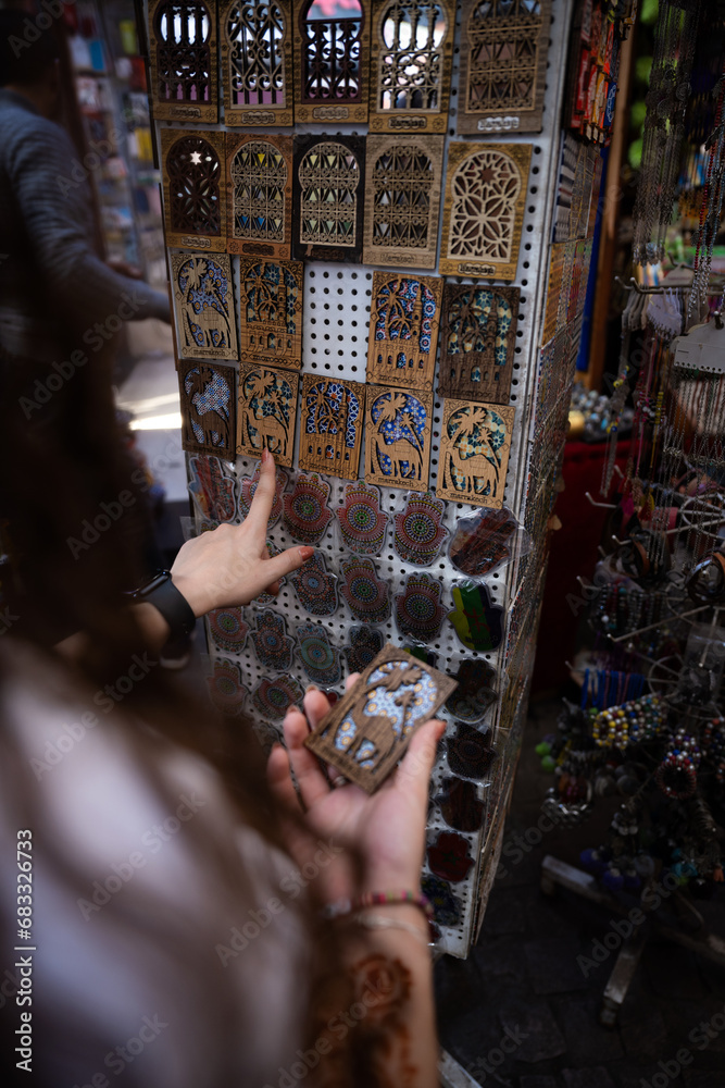(Selective focus) Defocused girl in the foreground choosing a magnet in Marrakesh's souk, Morocco. The souks of Marrakech are the largest in Morocco and famous globally.