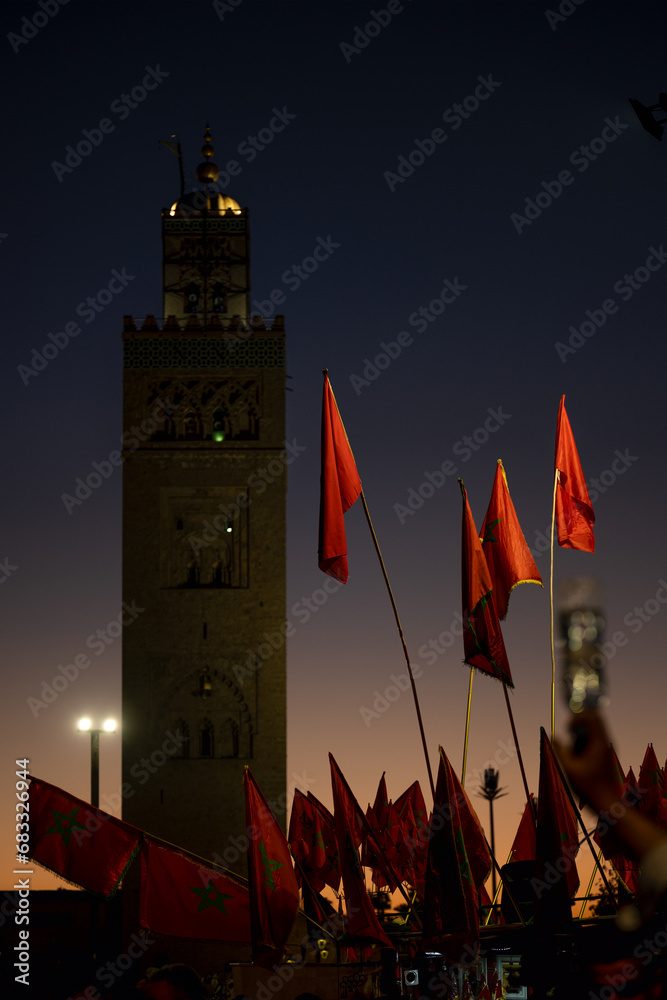 (Selective focus) Stunning view of some Moroccan flags in the foreground and defocused Kutubiyya Mosque in the background at sunset. Marrakesh, Morocco.