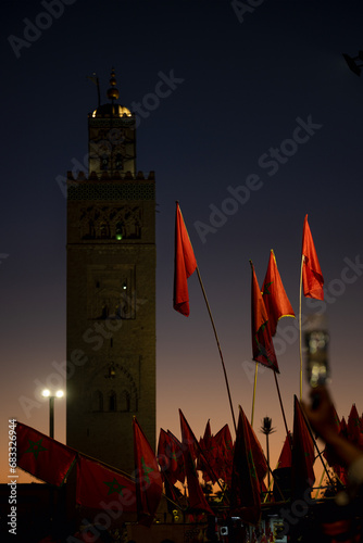Obraz na płótnie (Selective focus) Stunning view of some Moroccan flags in the foreground and defocused Kutubiyya Mosque in the background at sunset. Marrakesh, Morocco. w salonie