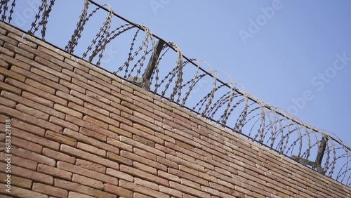 A brick wall with a security wire fence. Jail wall from above. Blue sky. Camp, freedom, war, forbidden, crime, security, protection, dangerous, control, escape concepts. (ID: 683327188)