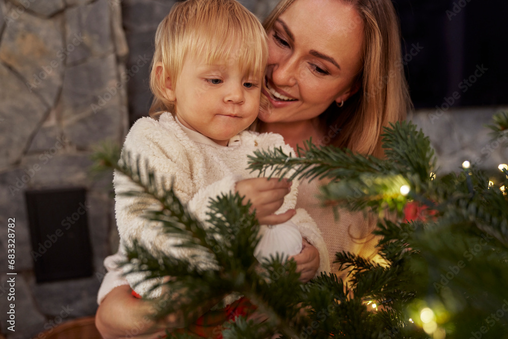 Mother carrying a toddler and standing next to the Christmas tree Mother carrying a toddler and standing next to the Christmas tree
