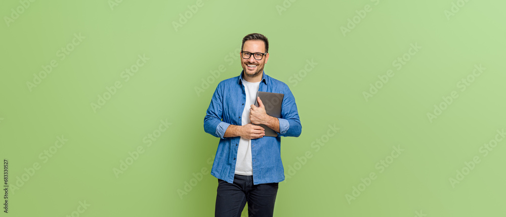 Portrait of handsome entrepreneur holding digital tablet and smiling at camera on green background - obrazy, fototapety, plakaty 