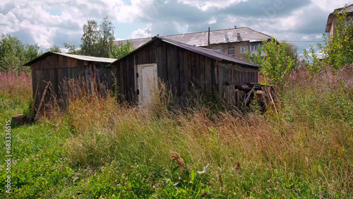 Old dark wooden small barn surrounded by green long grass. Clip. Sumer village background.