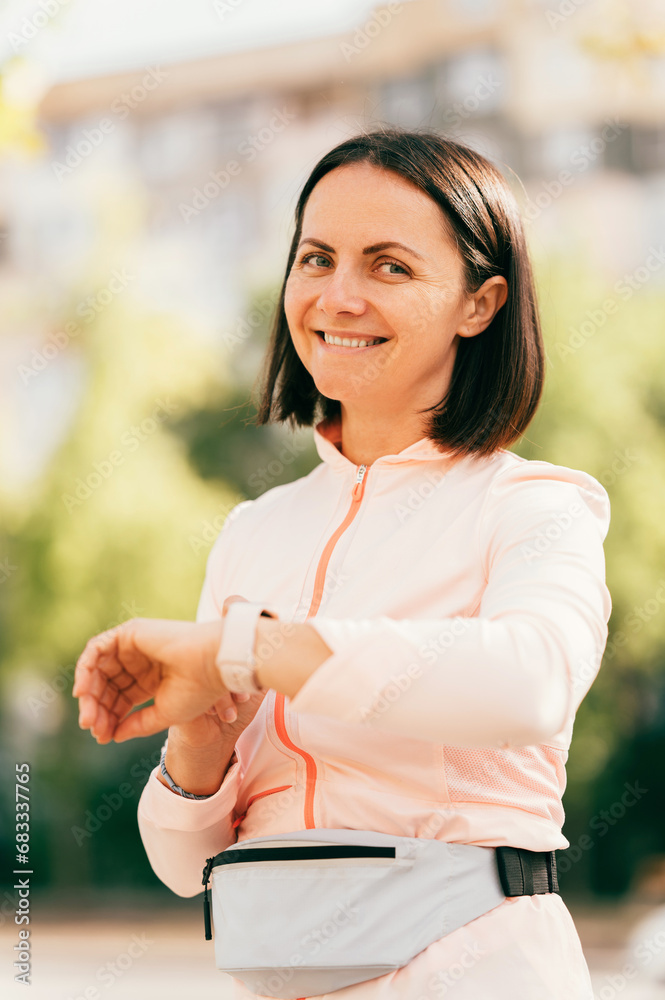 Close up vertical portrait shot of a middle age woman touching her smart watch and smiling at the camera.