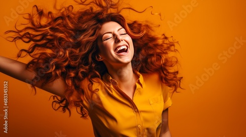 Bright young lady in a studio twisting her hair in a playful way; joyful woman dancing and rejoicing against an orange backdrop