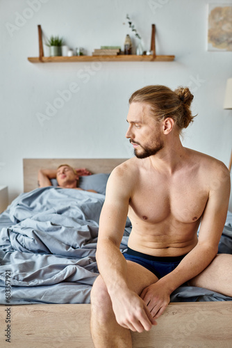 upset bearded man in underpants sitting on bed near sleeping love partner, troubled relationship