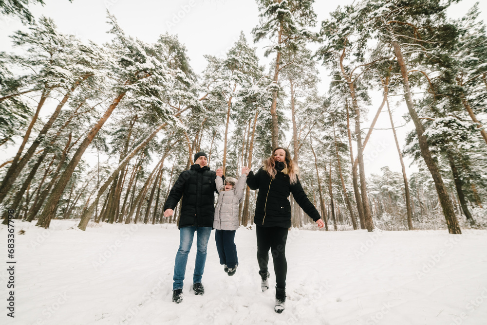 Mom, dad throws up child, playing in snow. Family in warm wear having fun and walking in winter forest. Father, mother, kid running in snowy woods, enjoying snowfall in park. Happy winter holidays. Mom, dad throws up child, playing in snow. Family in warm wear having fun and walking in winter forest. Father, mother, kid running in snowy woods, enjoying snowfall in park. Happy winter holidays.