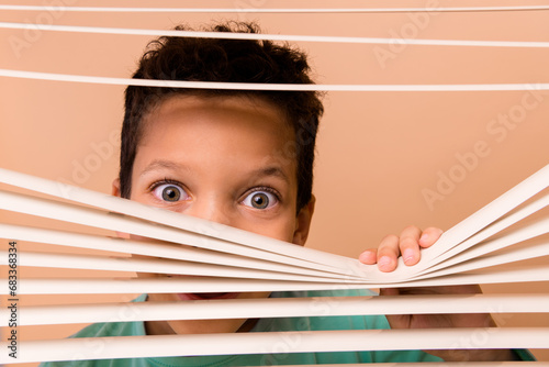 Portrait of schoolchild open look through window shutter jalousie isolated on beige color background photo