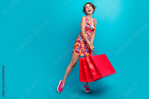 Full size photo of impressed woman dressed colorful clothes look at sale empty space hold new outfit isolated on blue color background photo