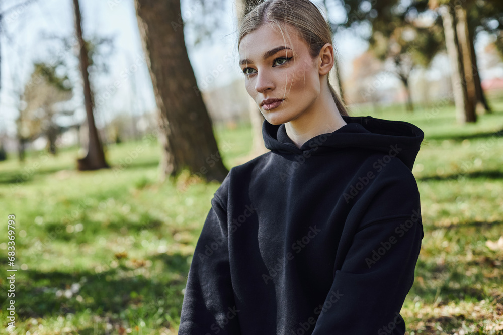 portrait of sportive young woman in black hoodie looking away in green park, nature and sport portrait of sportive young woman in black hoodie looking away in green park, nature and sport