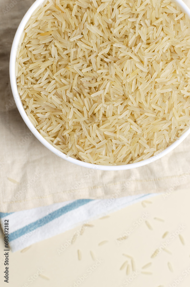 Raw basmati rice in a white bowl with a wooden spoon on a light background. Concept of Water-Conserving Products. Saving water. Healthy Eating. Vertical orientation. Top view. Copy space. Raw basmati rice in a white bowl with a wooden spoon on a light background. Concept of Water-Conserving Products. Saving water. Healthy Eating. Vertical orientation. Top view. Copy space.