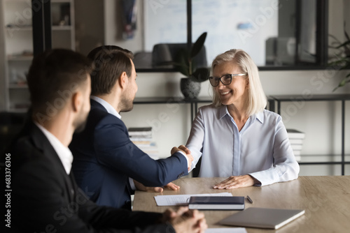 Positive confident younger and older business partners shaking hands on meeting, smiling, laughing, negotiating on contract, agreement, partnership. Senior team leader thanking employee with handshake © fizkes