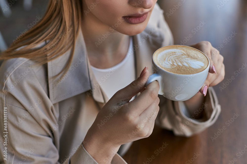 cropped blonde woman in trench coat enjoying her cup of cappuccino while sitting in cafe cropped blonde woman in trench coat enjoying her cup of cappuccino while sitting in cafe