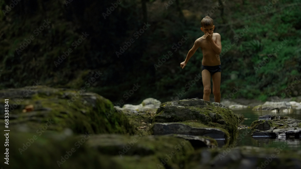 Fototapeta premium Boy walking on mossy rocks on green hills background. Creative. Teenager boy in jungles.