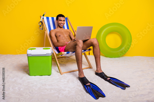 Full length photo of cool cheerful shirtless man relaxing lounge chair chatting twitter telegram facebook isolated yellow color background
