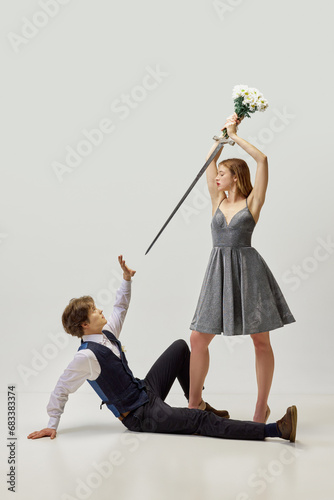 Queen of swords. baseless jealousy. Woman in cocktail dress stands over frightened man with his boyfriend with sword and bouquet of flowers. St. Valentine's day concept photo