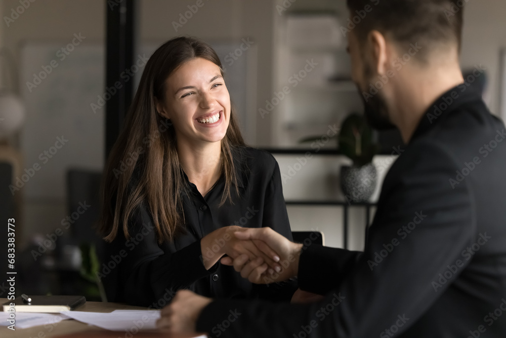 Happy pretty you business professional woman shaking hands with male colleague, smiling, laughing, enjoying teamwork, cooperation. Project managers, business partners giving handshake