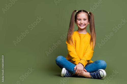 Full length photo of lovely kid dressed yellow sweatshirt denim pants sit near offer empty space isolated on khaki color background