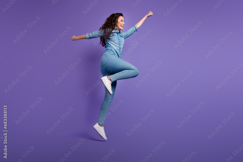 Full size profile portrait of overjoyed girl jump raise fist flying empty space isolated on purple color background