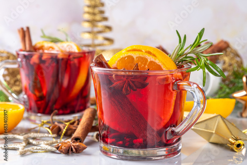Traditional Christmas aromatic mulled wine cocktail, red wine grog tea drink with spices, cinnamon, orange and rosemary sprig, on Christmas New Year decorated wooden cozy background