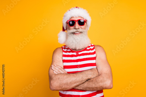 Photo of funky cheerful senior guy dressed christmas swimwear hat glasses arms crossed enjoy vacation isolated yellow color background © deagreez