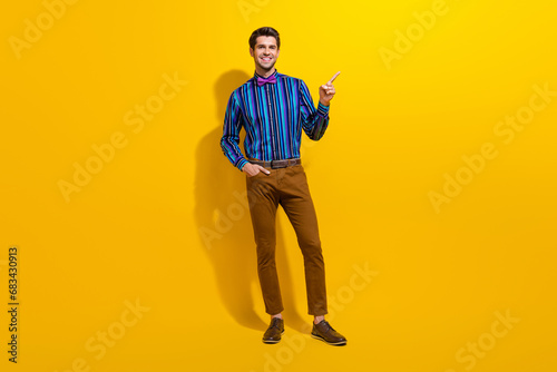 Full body photo of handsome man wear bow tie stylish shirt indicating at proposition empty space isolated on yellow color background © deagreez