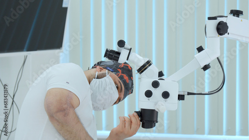 Ophthalmological surgery specialist in front of microscope before operation. Action. Side view of male doctor with medical equipment.